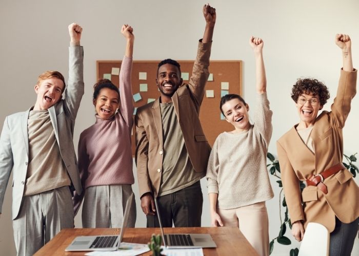 People with smiles and their fists in the air in victory after a successful group facilitation.